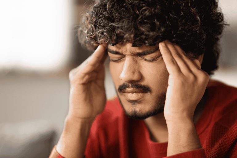 Young man placing his fingertips to his temples with his eyes closed, indicating a tension headache.